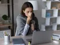 Chora kobieta z chusteczką przy nosie, otulona kocem, pracuje przy laptopie. Dyskutuje o swoim prawie do zasiłku chorobowego.
