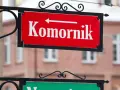 Czerwona tablica z napisem "Komornik" i strzałką w lewo. W tle budynek, może to być miejsce, gdzie zasiłek chorobowy jest zagrożony przez komornika.