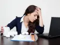 Zmęczona kobieta z kubkiem w dłoni, z ręką na czole, przed laptopem. Czy L4 w weekend się opłaca, gdy tak się czujesz?