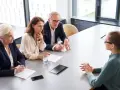 Biznesmeni dyskutują przy stole, czy od premii płaci się zus. Jedna z pań notuje.