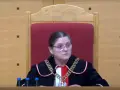 Sędzia w todze i łańcuchu na szyi, siedzi za stołem z butelkami wody. Czy sędziowie płacą składkę zdrowotną?