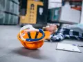 Pomarańczowy kask i notatnik leżą obok nieprzytomnego pracownika. To dowód na wypadek przy pracy, który może być podstawą do ubiegania się o świadczenia.