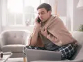Chory mężczyzna owinięty kocem rozmawia przez telefon, martwiąc się, czy sobota i niedziela wlicza się do chorobowego.