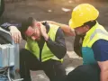 Pracownik z bólem szyi po wypadku przy pracy, wspierany przez kolegę. Zapewnienie świadczeń z tytułu wypadków przy pracy jest kluczowe.