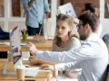 Dwóch współpracowników dyskutuje przy komputerze, analizując dane. Czy bezrobocie wlicza się do lat pracy? To pytanie nurtuje wielu.