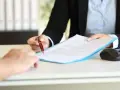 Podpisanie umowy na zastępstwo, gdy pracownik jest na L4. Dłoń z długopisem podaje dokument.