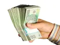 Dłoń trzyma plik banknotów 100 zł. Taka kwota z ubezpieczenia chorobowego przysługuje w wielu sytuacjach.