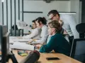 Zespół pracuje nad projektem. Mężczyzna pochyla się nad kobietą, wyjaśniając coś. To przykład, co to jest pracownik najemny.