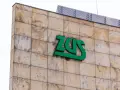 Zielone logo ZUS na beżowej, kamiennej elewacji. Czy chorobowe wlicza się do lat pracy? Zapytaj w ZUS.