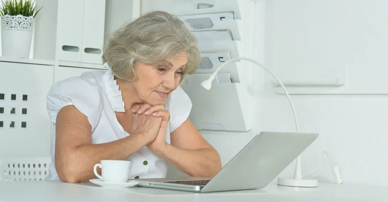 Starsza pani z zaciekawieniem patrzy na ekran laptopa, zastanawiając się, ile trwa staż.