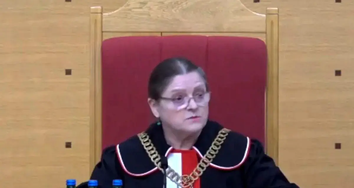 Sędzia w todze i łańcuchu na szyi, siedzi za stołem z butelkami wody. Czy sędziowie płacą składkę zdrowotną?