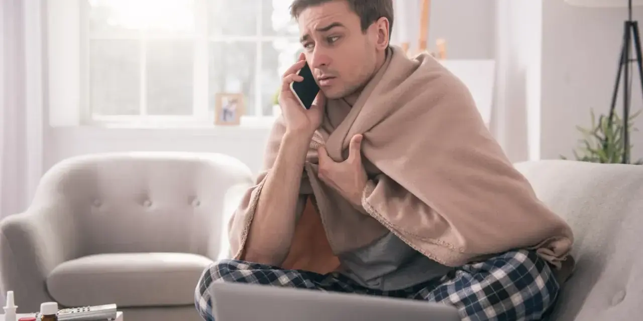 Chory mężczyzna owinięty kocem rozmawia przez telefon, martwiąc się, czy sobota i niedziela wlicza się do chorobowego.