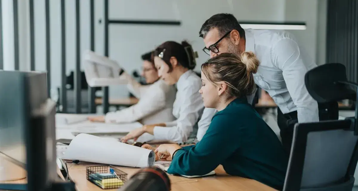 Zespół pracuje nad projektem. Mężczyzna pochyla się nad kobietą, wyjaśniając coś. To przykład, co to jest pracownik najemny.