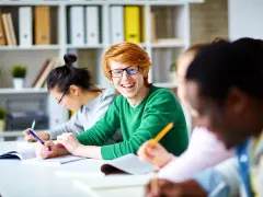 Uśmiechnięty rudowłosy student z okularami, piszący notatki. Czy szkoła zawodowa wlicza się do stażu pracy?