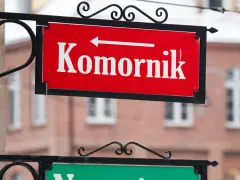Czerwona tablica z napisem "Komornik" i strzałką w lewo. W tle budynek, może to być miejsce, gdzie zasiłek chorobowy jest zagrożony przez komornika.