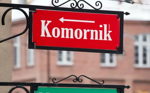 Czerwona tablica z napisem "Komornik" i strzałką w lewo. W tle budynek, może to być miejsce, gdzie zasiłek chorobowy jest zagrożony przez komornika.