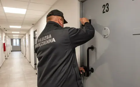 Strażnik więzienny przy drzwiach celi nr 23. Czy pobyt w zakładzie karnym wlicza się do emerytury? To pytanie nurtuje wielu.