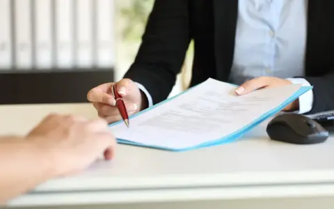 Podpisanie umowy na zastępstwo, gdy pracownik jest na L4. Dłoń z długopisem podaje dokument.