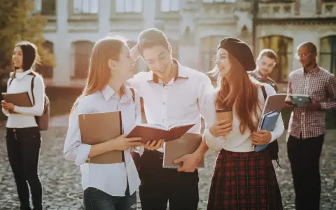 Studenci rozmawiający na kampusie, z książkami i notatkami w rękach. Wszyscy wyglądają na szczęśliwych, jakby właśnie skończyli zajęcia. To idealny obrazek dla osób, które chcą połączyć pracę z nauką, wybierając l4 a studia zaoczne.