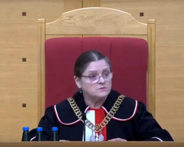 Sędzia w todze i łańcuchu na szyi, siedzi za stołem z butelkami wody. Czy sędziowie płacą składkę zdrowotną?