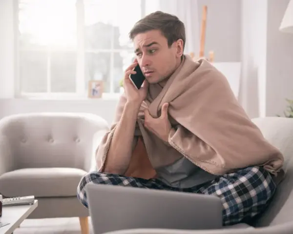 Chory mężczyzna owinięty kocem rozmawia przez telefon, martwiąc się, czy sobota i niedziela wlicza się do chorobowego.