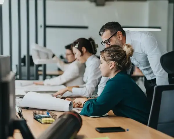 Zespół pracuje nad projektem. Mężczyzna pochyla się nad kobietą, wyjaśniając coś. To przykład, co to jest pracownik najemny.