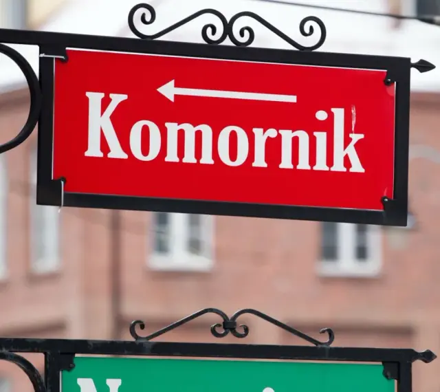 Czerwona tablica z napisem "Komornik" i strzałką w lewo. W tle budynek, może to być miejsce, gdzie zasiłek chorobowy jest zagrożony przez komornika.