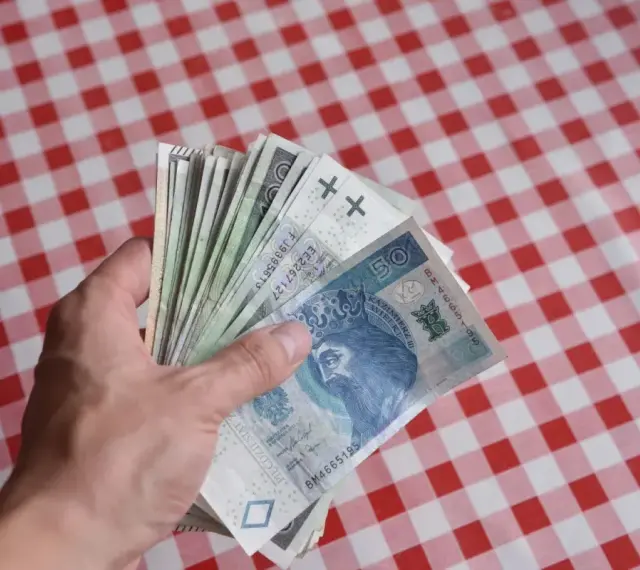 Dłoń trzyma plik polskich banknotów, symbolizujących kiedy dodatkowe pieniądze dla pracowników DPS.