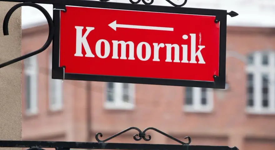 Czerwona tablica z napisem "Komornik" i strzałką w lewo. W tle budynek, może to być miejsce, gdzie zasiłek chorobowy jest zagrożony przez komornika.
