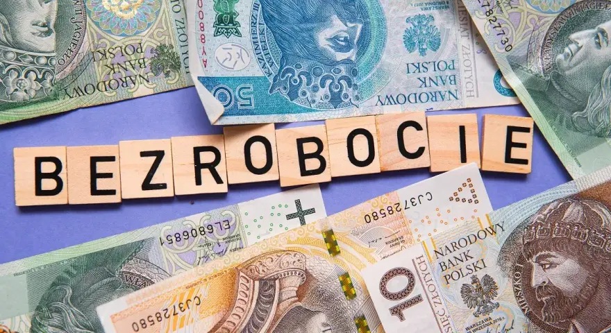 Litery układają się w słowo "BEZROBOCIE" na tle polskich banknotów. Zastanawiasz się, ile wynosi zasiłek dla bezrobotnych?