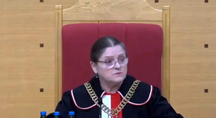 Sędzia w todze i łańcuchu na szyi, siedzi za stołem z butelkami wody. Czy sędziowie płacą składkę zdrowotną?