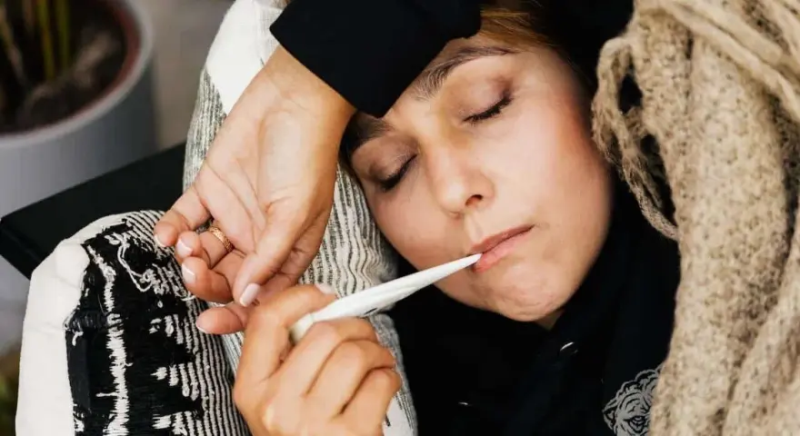 Kobieta z gorączką mierzy temperaturę. To ważny element przy ustalaniu podstawy wymiaru zasiłku chorobowego.