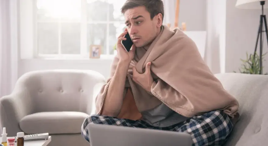 Chory mężczyzna owinięty kocem rozmawia przez telefon, martwiąc się, czy sobota i niedziela wlicza się do chorobowego.