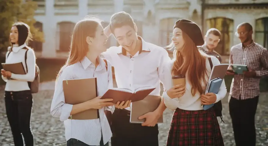 Studenci rozmawiający na kampusie, z książkami i notatkami w rękach. Wszyscy wyglądają na szczęśliwych, jakby właśnie skończyli zajęcia. To idealny obrazek dla osób, które chcą połączyć pracę z nauką, wybierając l4 a studia zaoczne.