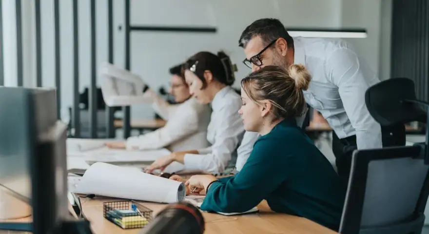 Zespół pracuje nad projektem. Mężczyzna pochyla się nad kobietą, wyjaśniając coś. To przykład, co to jest pracownik najemny.