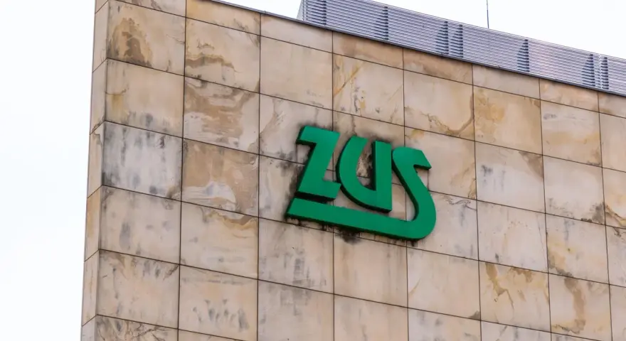Zielone logo ZUS na beżowej, kamiennej elewacji. Czy chorobowe wlicza się do lat pracy? Zapytaj w ZUS.