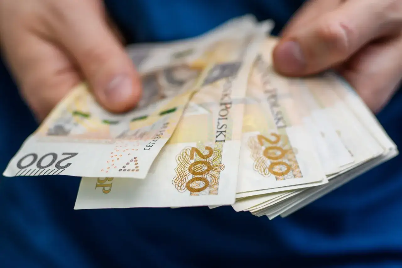Dłonie trzymają plik banknotów 200 zł. Zastanawiasz się, ile wynosi zasiłek dla bezrobotnych?