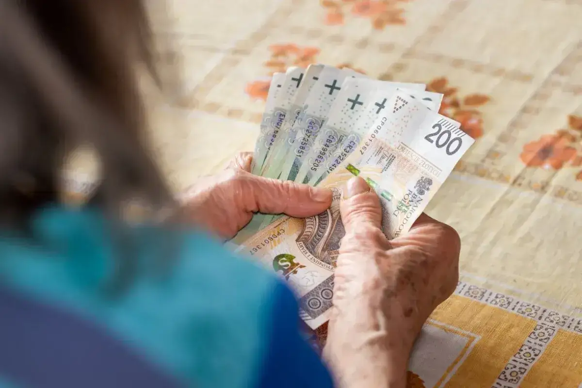 Dłonie emeryta liczą banknoty 200 zł. Nawet na zwolnieniu lekarskim, pracujący emeryt musi pilnować budżetu.