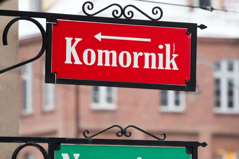 Czerwona tablica z napisem "Komornik" i strzałką w lewo. W tle budynek, może to być miejsce, gdzie zasiłek chorobowy jest zagrożony przez komornika.
