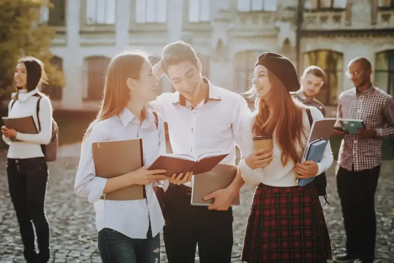 Studenci rozmawiający na kampusie, z książkami i notatkami w rękach. Wszyscy wyglądają na szczęśliwych, jakby właśnie skończyli zajęcia. To idealny obrazek dla osób, które chcą połączyć pracę z nauką, wybierając l4 a studia zaoczne.